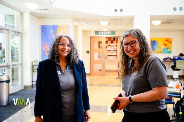Two women smiling and talking in a library or community center.