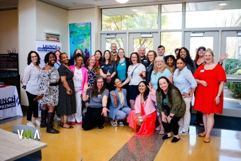 Group of diverse women and men gathered in a bright room for a photo.