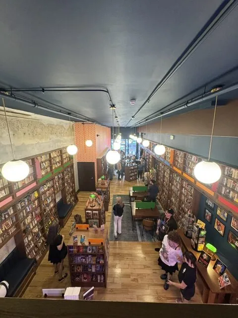 People browsing books in a cozy, well-lit bookstore with wooden floors and colorful decor.
