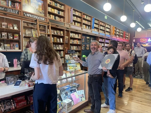 People browsing books in a bookstore with shelves and a counter in the background.