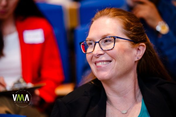 Smiling woman with glasses at an indoor event.