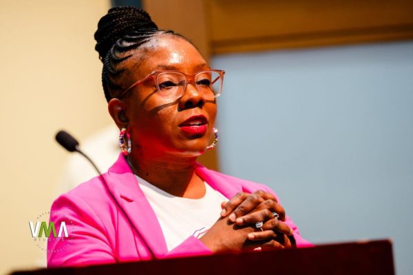 Woman with glasses and braided hair speaking at a podium.