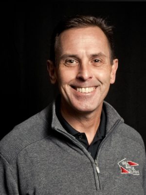 Smiling man in gray zip-up jacket with "De Garde Brewing" logo on chest.