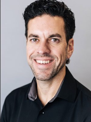 A smiling man with dark, curly hair wearing a black shirt.